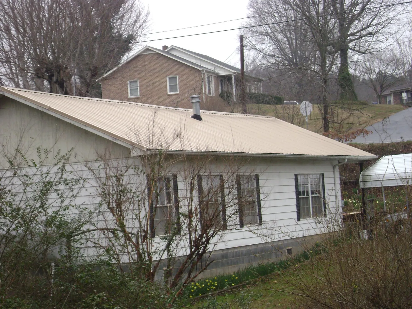 Tan metal roof on a white sided house set into a hillside — Commercial Roofing by Roofing Brothers in Franklin